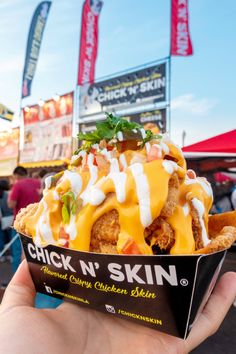 a person holding up a chicken n'skin sandwich in front of a crowd at an outdoor event