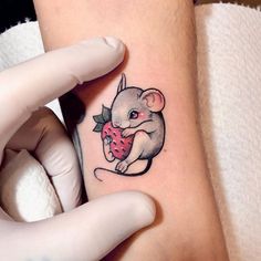 a small mouse holding a strawberry tattoo on the arm