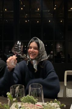 a woman sitting at a table with two wine glasses in front of her and smiling