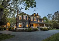 a large house with lots of windows and lights on it's front porch in the evening