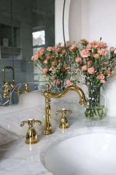 a marble sink with gold faucets and flowers in a vase on the counter