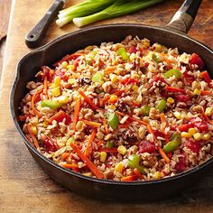 a pan filled with rice and vegetables on top of a wooden cutting board next to a knife