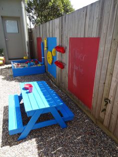 a blue picnic table sitting next to a red and yellow sign on a wooden fence