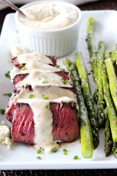 steak and asparagus on a white plate with sauce