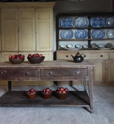 an old wooden table with bowls of fruit on it