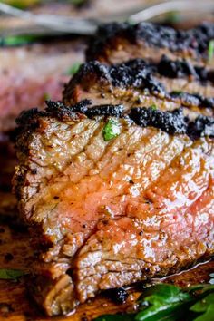 two pieces of steak on a cutting board with herbs and seasoning next to it