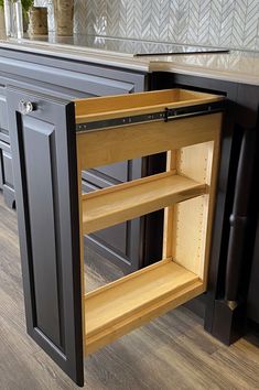 an open cabinet in the middle of a kitchen with wood flooring and black cabinets