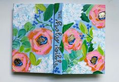 an open book with flowers painted on the pages and words written in blue, green, pink and white