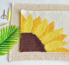 a crocheted placemat with a sunflower on it next to a green palm leaf