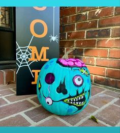 a painted pumpkin sitting on the ground next to a sign