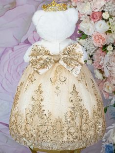 a white teddy bear wearing a gold dress with a crown on it's head