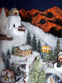 a christmas scene with houses and trees in the foreground, snow covered mountains behind