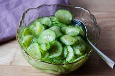 a bowl filled with cucumbers on top of a wooden table next to a purple napkin