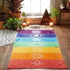 a rainbow colored rug in the middle of a room with potted plants and candles