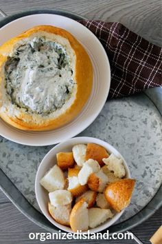 a bowl of spinach dip next to a plate of bread on a platter