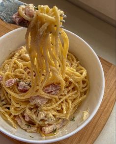 a person holding a fork full of pasta with ham and cheese on it in a white bowl