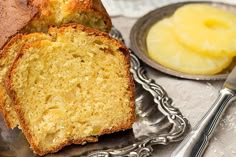 a loaf of banana bread sitting on top of a silver plate next to a bowl of fruit