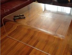 a glass coffee table with remotes on the wooden floor in front of a couch