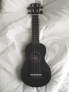 a black ukulele laying on top of a white sheet