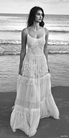 a black and white photo of a woman in a dress on the beach with waves behind her