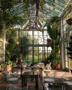 the inside of a glass house with tables and chairs in front of it, surrounded by greenery