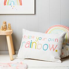 a pillow that says follow your own rainbow on it next to a small wooden stool