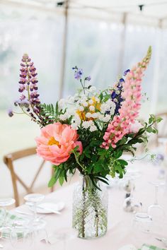 a vase filled with lots of flowers on top of a white table cloth covered table