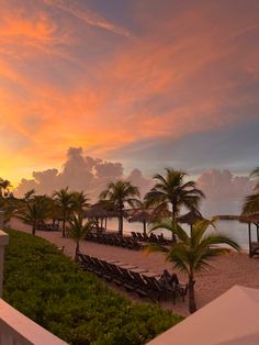 the sun is setting over an ocean with lounge chairs and palm trees on the beach