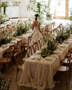 a woman standing in front of a long table covered with flowers and greenery at an event