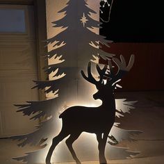 a paper cut out of a deer standing next to a christmas tree with lights on it