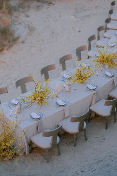 a long table set up on the beach with place settings