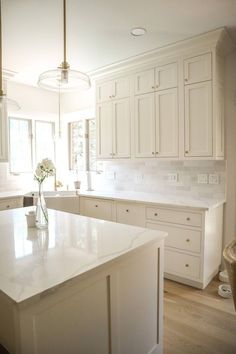 a large kitchen with white cabinets and an island in the middle is shown, along with a vase filled with flowers