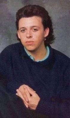 a young man in a blue sweater is posing for a photo with his hand on his chest