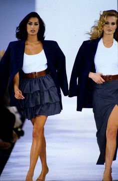 two women walking down the runway in skirts and jackets, with one woman wearing a white top