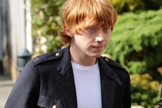 a young man with red hair wearing a black jacket and white t - shirt is walking down the street