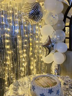 a birthday cake sitting on top of a table covered in balloons and confetti