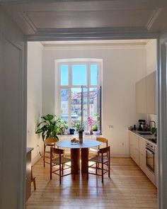 an open kitchen and dining room area with wooden flooring, white walls and windows