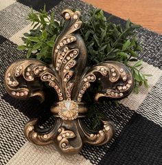 an ornate fleur de lis is sitting on a checkered tablecloth with greenery