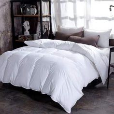 a bed with white comforter and pillows in a room next to a book shelf