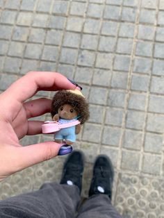 a person holding a small doll in their hand on the ground next to a brick walkway