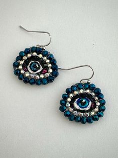 Handmade Evil Eye Nickel Free Earrings, featuring a blue embroidered eye surrounded by glass beads and rhinestones. Each Small Evil Eye is Approx. approx. 1 inches W x .75 inches H. and includes a nickel free earring hook and leather back.  The evil eye is a curse thought to be given by a malicious glare that can cause bad luck or loss. Wearing the evil eye wards of the curse protecting you throughout your day.   Handmade by a high school art teacher and a woman owned small business. Details: - Materials The Evil Eye is made of embroidery floss, rhinestones and Japanese beads. Back side is covered by faux leather. The earring hook does not contain nickel. - Care Tips Please handle with care and store carefully when not being worn. Avoid spraying perfumes, don't put it into water, and avoid Beaded Embroidery Earrings, High School Art Teacher, Handmade Evil Eye, Japanese Beads, Ethiopian Opal Ring, Earring Hook, Nickel Free Earrings, Luck Charm, Bad Luck