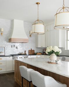 a kitchen with white cabinets and marble counter tops, two pendant lights hanging over the island