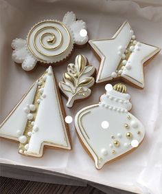 decorated christmas cookies in a box on a table with white and gold trimmings