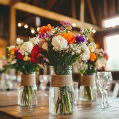 colorful flowers in mason jars on a table with wine glasses and place settings for the guests to sit at