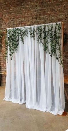 a white curtain with green plants on it in front of a brick wall and wooden bench