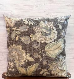 a brown pillow with flowers on it sitting on top of a wooden table next to a white wall