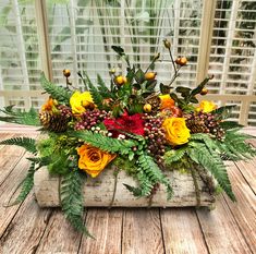 an arrangement of flowers and greenery in a wooden box on a table next to a window