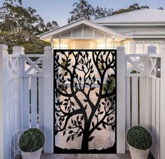 a gate with a tree cut out on the top and bottom, surrounded by potted plants