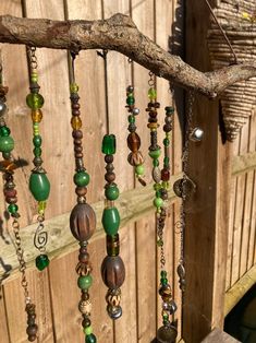 a tree branch with beads hanging from it's side next to a wooden fence