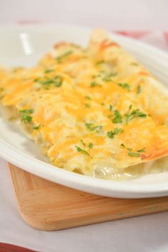 a white plate topped with cheesy potatoes on top of a wooden cutting board